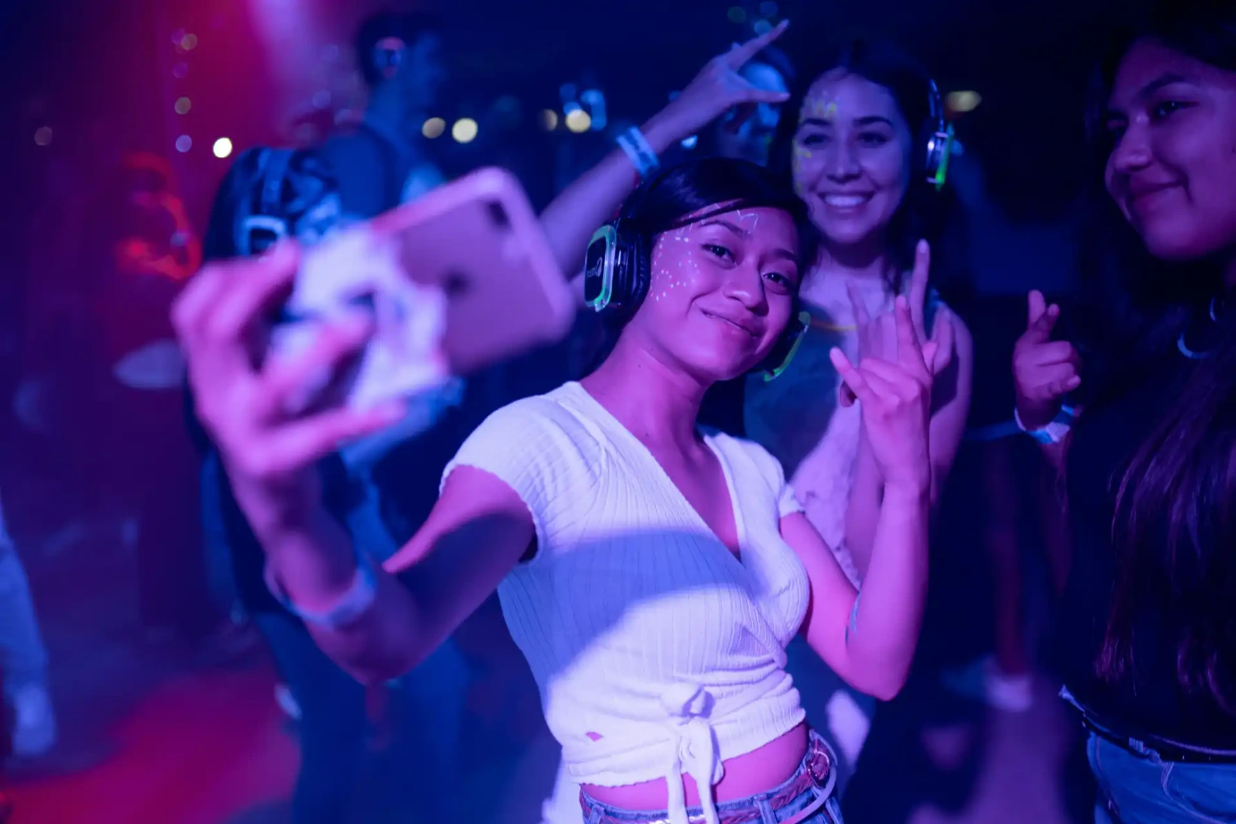 Een groepje jongeren is al dansend een selfie aan het nemen op een feestje. Op hun hoofd hebben ze allemaal een hoofdtelefoon.