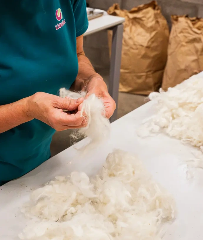 Een medewerker van Lidwina is de schapenwol van MolWol aan het verwerken tot zakjes schapenwolvulling voor Maak een Beer